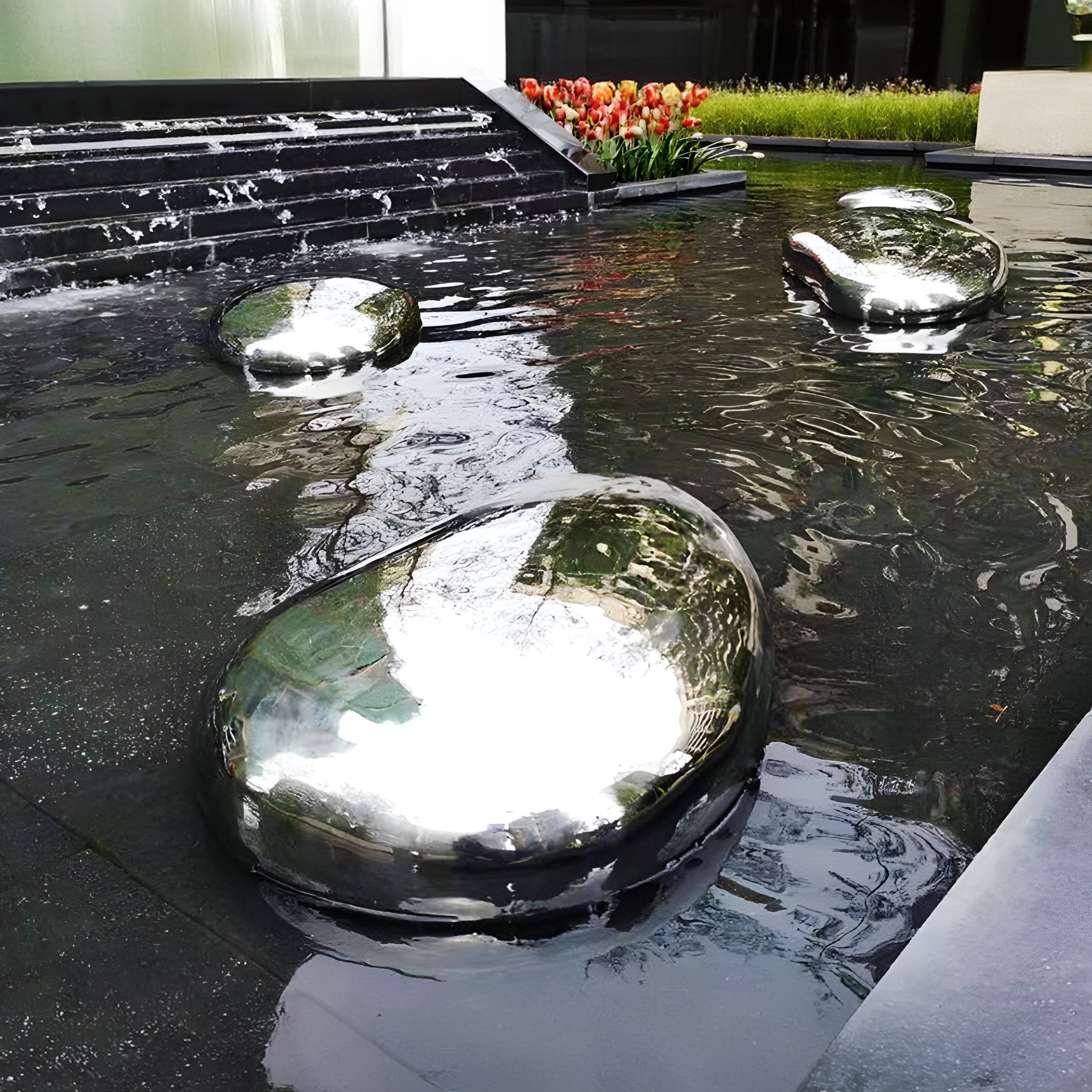 Reflective pebble stainless steel sculptures placed in a water feature, complementing a modern garden landscape.