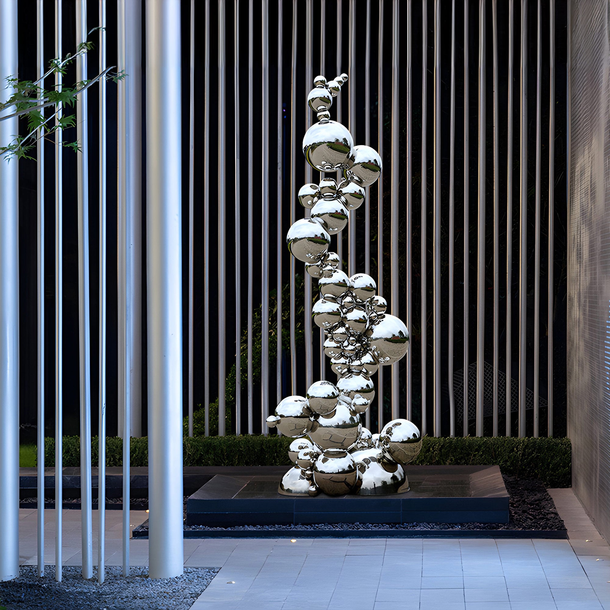 Outdoor stainless steel sculpture featuring a vertical arrangement of reflective spheres, creating a striking modern art piece in a sleek garden setting.